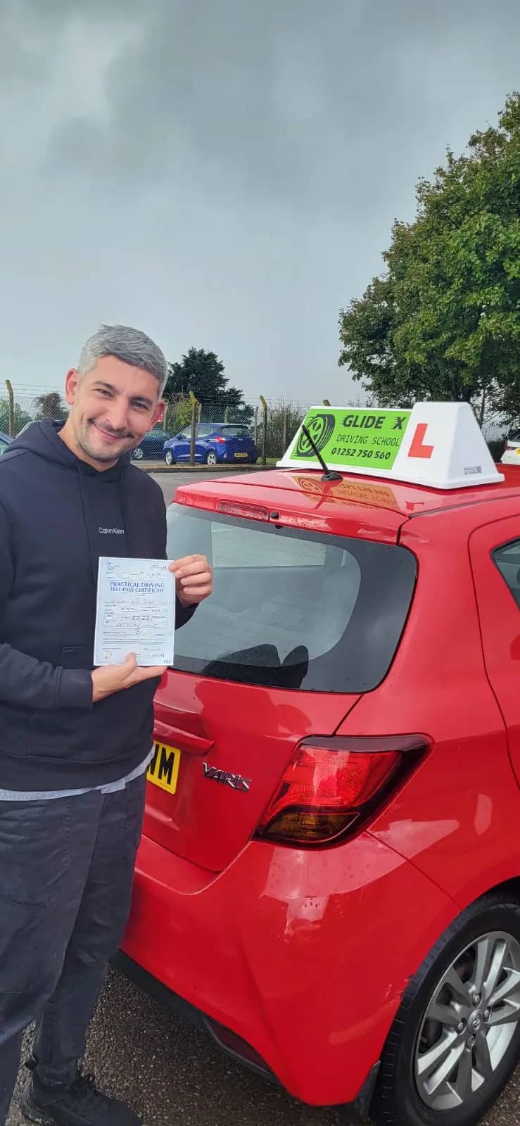 GlideX pupil holding a practical driving test pass certificate beside the GlideX dual-control car